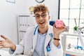 Young caucasian doctor man wearing doctor uniform holding piggy bank at the clinic celebrating achievement with happy smile and Royalty Free Stock Photo