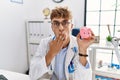 Young caucasian doctor man wearing doctor uniform holding piggy bank at the clinic covering mouth with hand, shocked and afraid Royalty Free Stock Photo