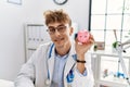 Young caucasian doctor man wearing doctor uniform holding piggy bank at the clinic looking positive and happy standing and smiling Royalty Free Stock Photo