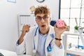 Young caucasian doctor man wearing doctor uniform holding piggy bank at the clinic scared and amazed with open mouth for surprise, Royalty Free Stock Photo