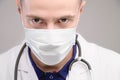 A young Caucasian doctor wearing a mask looks ominously into the camera from under his brow. Medical conspiracy concept