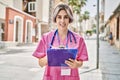 Young caucasian doctor woman smiling happy writing on clipboard at the city