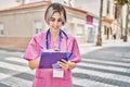 Young caucasian doctor woman smiling happy writing on clipboard at the city
