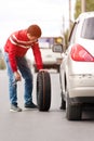 Young caucasian driver changing tyre wheel on road