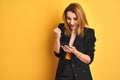 Young caucasian elegant business woman using smartphone over isolated yellow background screaming proud and celebrating victory Royalty Free Stock Photo