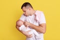 Young Caucasian father gives to baby soother, looking at her daughter or son with great love, guy wearing white t shirt, posing