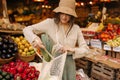 Young caucasian female shopper packs fresh vegetables in shopping bag standing at market.