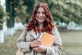 University young caucasian female student wearing glasses with books outside campus. Fiery curly hair Royalty Free Stock Photo