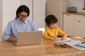 Young caucasian female work on laptop as son draws. Remote home office at covid-19 lockdown concept Royalty Free Stock Photo