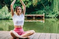 Young caucasian fitness woman doing yoga, meditate outdoors, on wooden pier lake on summer day