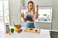 Young caucasian fitness woman wearing sportswear preparing healthy salad at the kitchen annoyed and frustrated shouting with