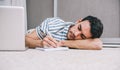 Young Caucasian freelancer business man sleeping near to laptop with eyes closed while lying on the floor home and notice paper. Royalty Free Stock Photo