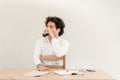 Young, Caucasian freelancer man sitting in his home office at the table, drinking coffee in front of empty clear wall. Royalty Free Stock Photo