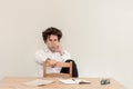 Young, Caucasian freelancer man sitting in his home office at the table, drinking water in front of empty clear wall. Royalty Free Stock Photo