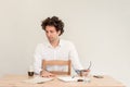 Young, Caucasian freelancer man sitting in his home office at the table in front of empty clear wall. Royalty Free Stock Photo