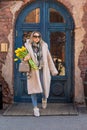 A young Caucasian girl comes out of the door of a cafe or shop with a bouquet of spring flowers. Royalty Free Stock Photo