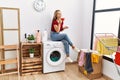 Young caucasian girl drinking coffee waiting for laundry sitting on whasing machine at home Royalty Free Stock Photo