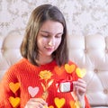 Young caucasian girl holding a white gift box with red ribbon and gold rose at home, decorated with bokeh Royalty Free Stock Photo