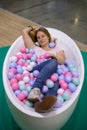 Young caucasian girl is lying in the bath with multi-colored plastic balls and smiling with closed eyes. holds a ball in Royalty Free Stock Photo