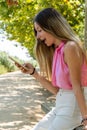 Young caucasian girl with a pink top elated while looking at her phone