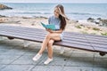 Young caucasian girl reading book sitting on the bench at the beach Royalty Free Stock Photo