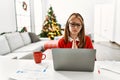 Young caucasian girl sitting on the table working using laptop by christmas tree begging and praying with hands together with hope Royalty Free Stock Photo