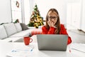 Young caucasian girl sitting on the table working using laptop by christmas tree looking stressed and nervous with hands on mouth Royalty Free Stock Photo