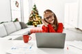 Young caucasian girl sitting on the table working using laptop by christmas tree sleeping tired dreaming and posing with hands