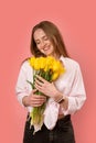 Young caucasian girl smiling and holding bunch of yellow tulips in her hands isolated on pink background. Vertical frame Royalty Free Stock Photo