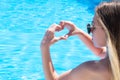 Young caucasian girl in sunglasses is holding hands in heart shaped on background of swimming pool with blue water in hotel. Royalty Free Stock Photo