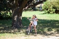 Young Caucasian girl trying to ride her bicycle in summer park on meadow with green grass Royalty Free Stock Photo