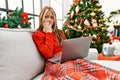 Young caucasian girl using laptop sitting on the sofa by christmas tree looking stressed and nervous with hands on mouth biting Royalty Free Stock Photo