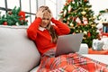 Young caucasian girl using laptop sitting on the sofa by christmas tree suffering from headache desperate and stressed because Royalty Free Stock Photo