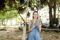 Young caucasian girl using tablet and riding swing on sand, wearing jeans sundress. Royalty Free Stock Photo