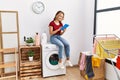 Young caucasian girl using touchpad waiting for laundry sitting on whasing machine at home Royalty Free Stock Photo