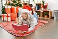 Young caucasian girl wearing christmas hat reading book lying on the floor at home Royalty Free Stock Photo