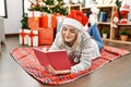 Young caucasian girl wearing christmas hat reading book lying on the floor at home Royalty Free Stock Photo