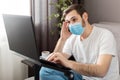 Young caucasian gloomy man in stress working from home office wearing protective mask using laptop and internet. Coronavirus covid Royalty Free Stock Photo