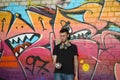 Young caucasian graffiti artist in black t-shirt with silver aerosol spray can near colorful graffiti in pink tones on brick wall Royalty Free Stock Photo