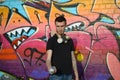 Young caucasian graffiti artist in black t-shirt with silver aerosol spray can near colorful graffiti in pink tones on brick wall Royalty Free Stock Photo