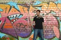 Young caucasian graffiti artist in black t-shirt with silver aerosol spray can near colorful graffiti in pink tones on brick wall Royalty Free Stock Photo