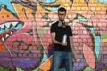 Young caucasian graffiti artist in black t-shirt with silver aerosol spray can near colorful graffiti in pink tones on brick wall Royalty Free Stock Photo
