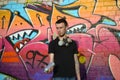 Young caucasian graffiti artist in black t-shirt with silver aerosol spray can near colorful graffiti in pink tones on brick wall Royalty Free Stock Photo