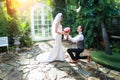 Young caucasian groom is kneeling and giving asian bride bouquet with eyes contact and happy smiling face during wedding or pre