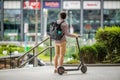 Young caucasian guy holding electric scooter, standing on a dais, planning optimal route in big modern city bypassing traffic jams Royalty Free Stock Photo