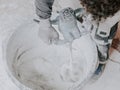 A young caucasian guy a plasterer holds a construction electric mixer and stirs dry putty with water Royalty Free Stock Photo