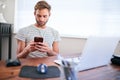 Young caucasian guy using phone while sitting at his desk Royalty Free Stock Photo