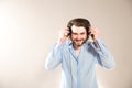 Young caucasian handsome man with a beard  putting on black headphones, wearing a blue shirt on gray Royalty Free Stock Photo