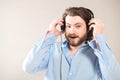 Young caucasian handsome man with a beard  putting on black headphones, wearing a blue shirt on gray Royalty Free Stock Photo