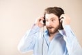 Young caucasian handsome man with a beard  putting on black headphones, wearing a blue shirt on gray Royalty Free Stock Photo